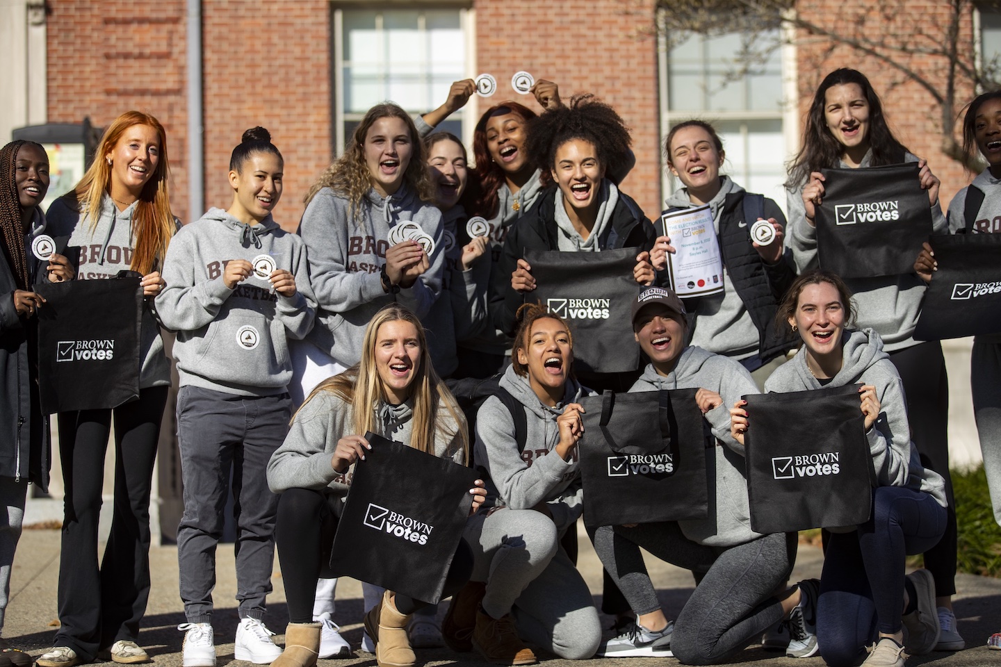 group photo of students in brown university sweatshirts holding brown votes tote bags