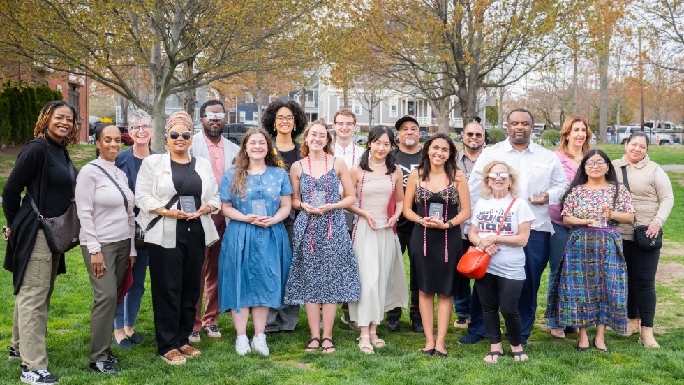 All award recipients pose, standing together outside in a group and smiling directly at the camera.