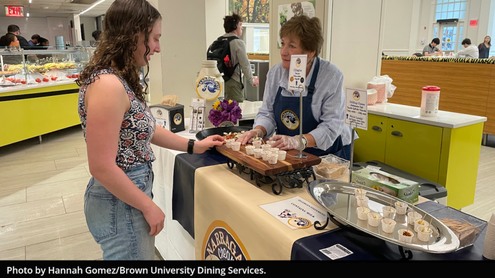Two people smiling and standing at a Narragansett Creamery sample table.