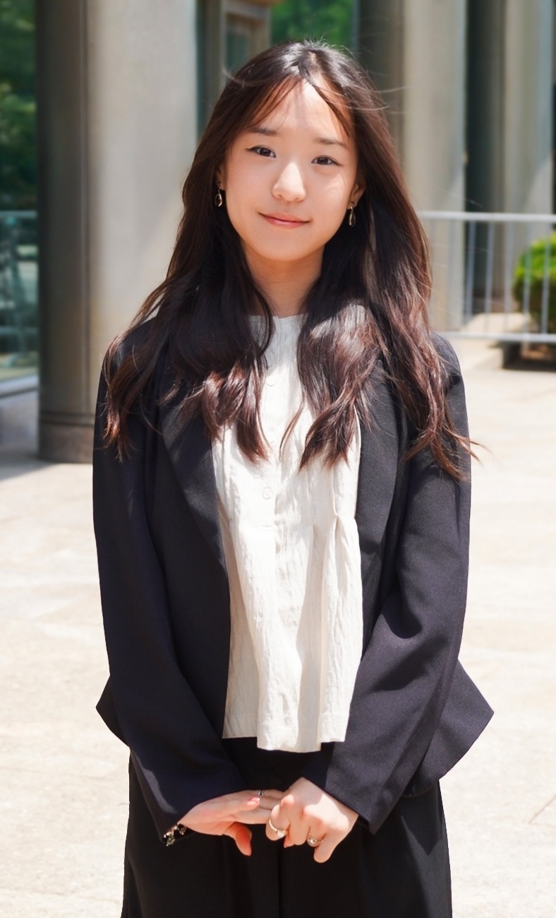 Cat Geo stands outdoors in front of a building wearing a black blazer and white blouse.